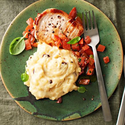 Ein grüner Teller mit würzigem Mini-Schnitzel, Kartoffel-Butter-Stampf, garniert mit gewürfelten Tomaten und frischem Basilikum. Rechts liegen Gabel und Messer, alles auf einer grünen Stoffserviette.