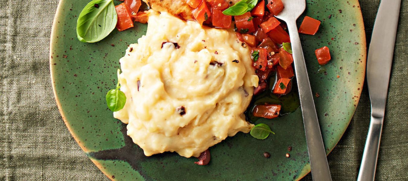 Ein grüner Teller mit würzigem Mini-Schnitzel, Kartoffel-Butter-Stampf, garniert mit gewürfelten Tomaten und frischem Basilikum. Rechts liegen Gabel und Messer, alles auf einer grünen Stoffserviette.