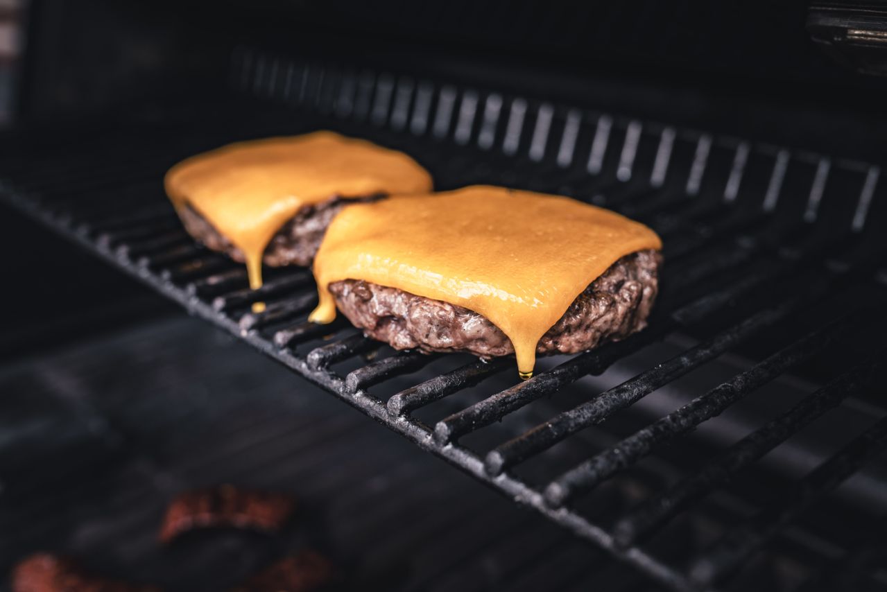 Zwei Rindfleisch-Burger-Patties mit geschmolzenem Cheddar-Käse werden auf einem Grillrost gegrillt.