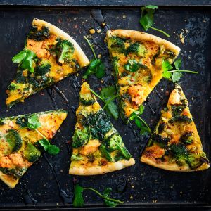 Fünf Stücke Gemüsepizza, die an eine Gemüsequiche erinnern, werden mit Brokkoli, Spinat, Käse und frischem Koriander auf einem dunklen Backblech belegt, wobei eine beträufelte Sauce und verstreute Kräuter für lebendige Farbe und Textur sorgen.
