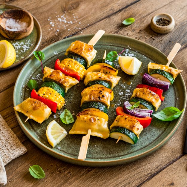 Drei Gemüsespieße mit Tofu, Zucchini, roten Zwiebeln und Paprika auf einem grünen Teller, garniert mit Zitronenspalten, Basilikum und einer Portion selbstgemachter Kräuterbutter – perfekt für alle, die Inspiration für ihr Kräuterbutter-Rezept suchen.
