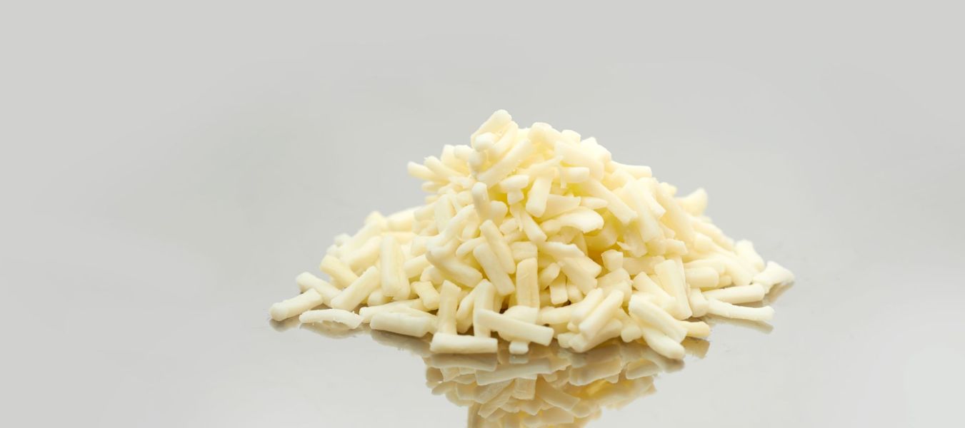 Ein kleiner Haufen geriebener Weißkäse, perfekt für Käseschmelzen, wird auf eine glatte, reflektierende Oberfläche mit einem schlichten hellgrauen Hintergrund gelegt.