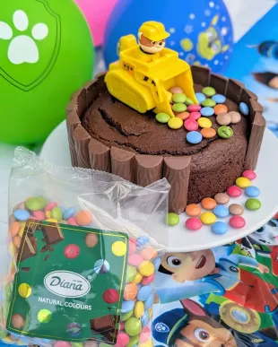 Ein Schokoladenkuchen, dekoriert mit überzogener Schokolade und einem Spielzeug-Bulldozer obendrauf, kreiert von mrs_supermum, umgeben von Luftballons mit Paw-Patrol-Motiven und einer Tüte mit bunten Süßigkeiten