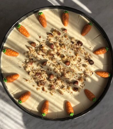Ein runder, köstlicher Kuchen, garniert mit kleinen Marzipankarotten am Rand und in der Mitte verstreut mit gehackten Nüssen, fotografiert im natürlichen Sonnenlicht.