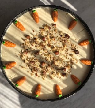 Ein runder, köstlicher Kuchen, garniert mit kleinen Marzipankarotten am Rand und in der Mitte verstreut mit gehackten Nüssen, fotografiert im natürlichen Sonnenlicht.