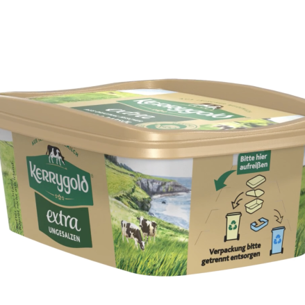 Ein rechteckiger Becher ungesalzener Kerrygold Extra Butter mit goldenem Deckel. Die Verpackung zeigt grüne Felder, Kühe und Recyclingsymbole, deutschen Text und hebt die Produktkategorie Streichfette mit einem malerischen Landschaftsbild hervor.