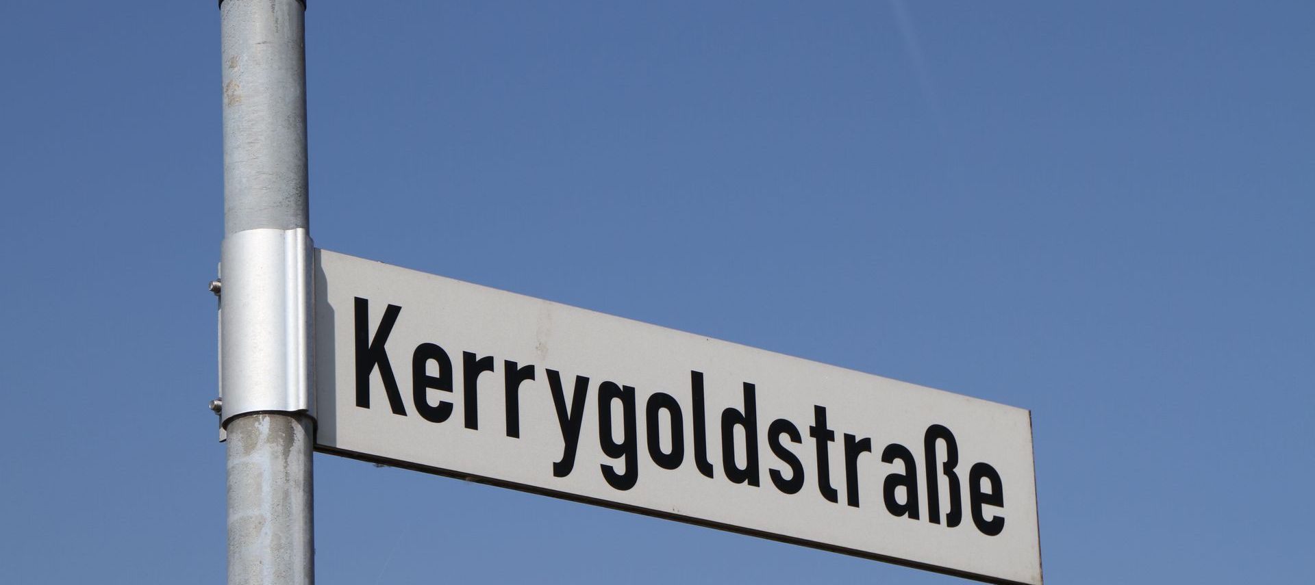 Ein Straßenschild mit der Aufschrift Kerrygoldstraße vor einem strahlend blauen Himmel.
