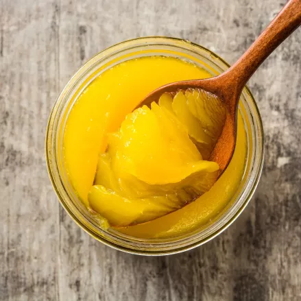Ein Holzlöffel, der leuchtend gelbes Ghee aus einem Glasgefäß schöpft, das auf einer rustikalen Holzfläche steht - eine wesentliche Zutat in der ayurvedischen Küche.
