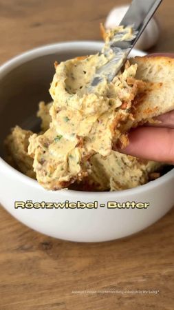 Ein Messer streicht Röstzwiebelbutter auf eine Scheibe Brot, im Hintergrund eine Schale mit der Butter. Der Text auf dem Bild lautet Röstzwiebel - Butter.