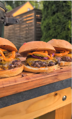 Drei Cheeseburger mit geschmolzenem Käse und Zwiebeln sind auf einer hölzernen Fläche im Freien aufgereiht.