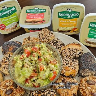 Eine Schale mit Guacamole ist umgeben von verschiedenen Brötchen auf einem Teller. Hinter dem Teller stehen Becher mit Kerrygold Frischkäseaufstrichen.