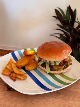 Ein Cheeseburger mit Salat im Brötchen wird auf einem gestreiften Teller serviert, dazu gibt es knusprige Wedge Fries und Chicken Nuggets.