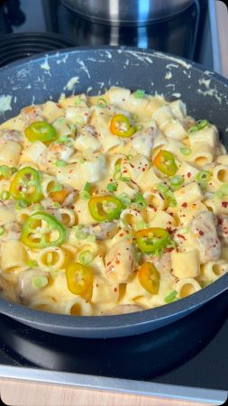 Eine Nahaufnahme einer mit cremiger Pasta gefüllten Pfanne von bbqdad85, garniert mit in Scheiben geschnittenen grünen Chilischoten, gehackten grünen Zwiebeln und roten Pfefferflocken. Die Nudeln sind mit Hähnchenstücken durchsetzt.