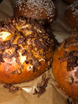 Nahaufnahme von frisch gebackenen Laugenbrötchen mit goldbrauner Kruste, teilweise mit knusprigen Röstzwiebeln oder Sesam bestreut.