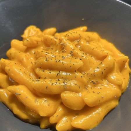 Ein Teller mit Kürbis-Mac and Cheese: Pasta in cremiger, orangefarbener Kürbis-Käsesauce, garniert mit frischen Kräutern.