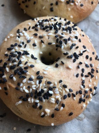 Nahaufnahme eines goldbraun gebackenen Bagels mit schwarzem und weißem Sesam, auf Backpapier liegend.