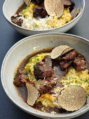 Zwei Teller mit geschmortem Rindfleisch auf cremigem Kartoffelpüree, garniert mit Trüffelscheiben und frischen Kräutern.