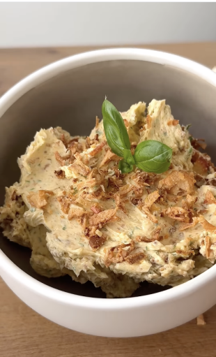 Weiße Schüssel mit einer Portion Kräuterbutter, garniert mit knusprigen Röstzwiebeln und einem frischen Basilikumblatt.