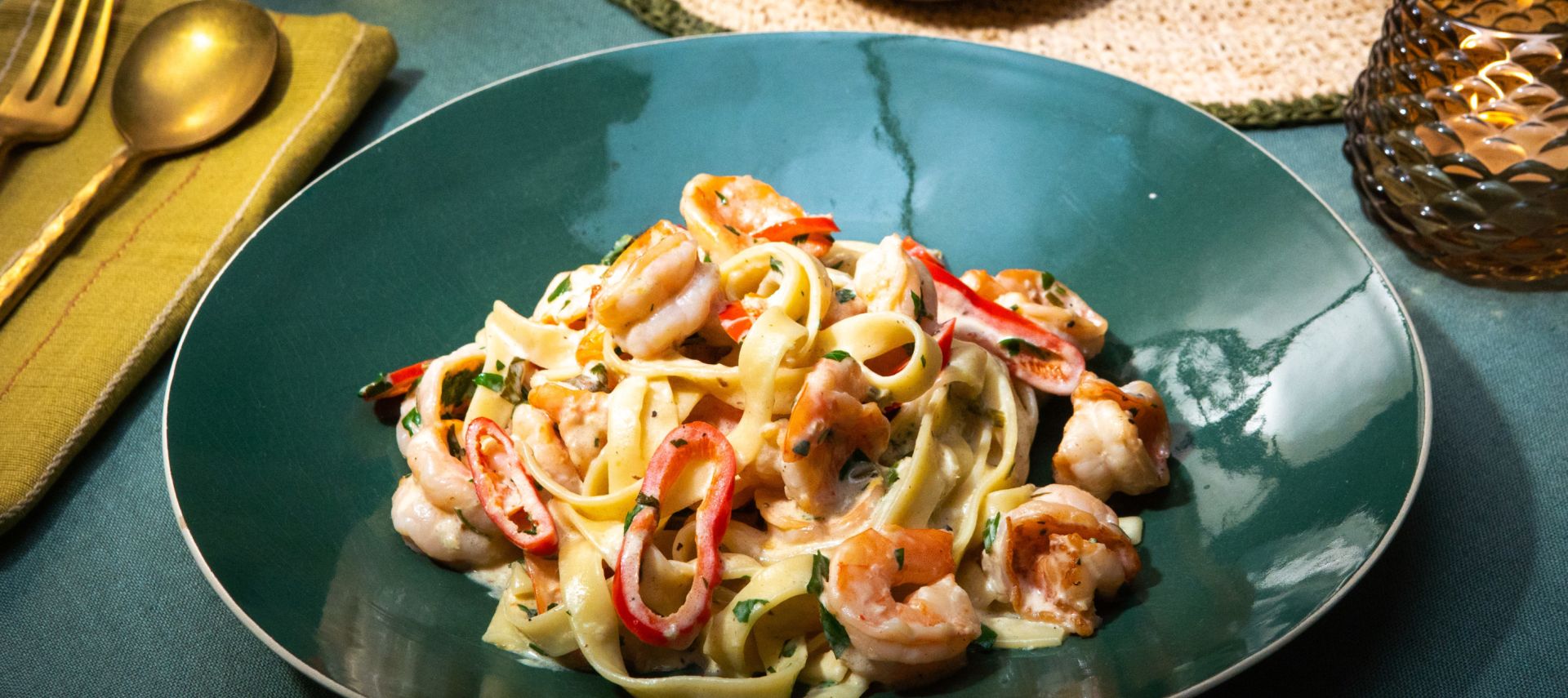 Ein grüner Teller mit Tagliatelle in cremiger Sauce, serviert mit Garnelen, roten Chilistreifen und frischer Petersilie.