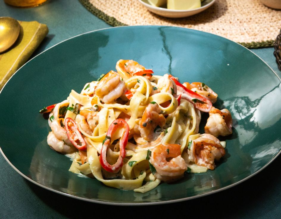 Ein grüner Teller mit Tagliatelle in cremiger Sauce, serviert mit Garnelen, roten Chilistreifen und frischer Petersilie.