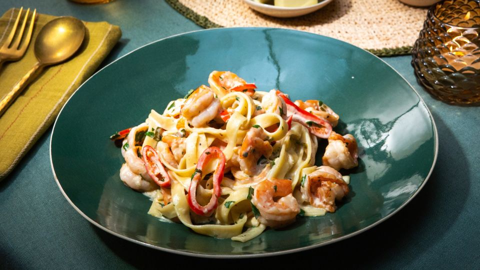 Ein grüner Teller mit Tagliatelle in cremiger Sauce, serviert mit Garnelen, roten Chilistreifen und frischer Petersilie.