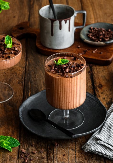 Zwei Gläser mit cremigem Schokoladenmousse, garniert mit dunklen Schokoladenraspeln und einem frischen Minzblatt.