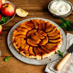 Ein rundes Apfel-Tarte-Tatin auf einem Keramikteller, belegt mit glänzend karamellisierten Apfelscheiben in konzentrischen Kreisen.
