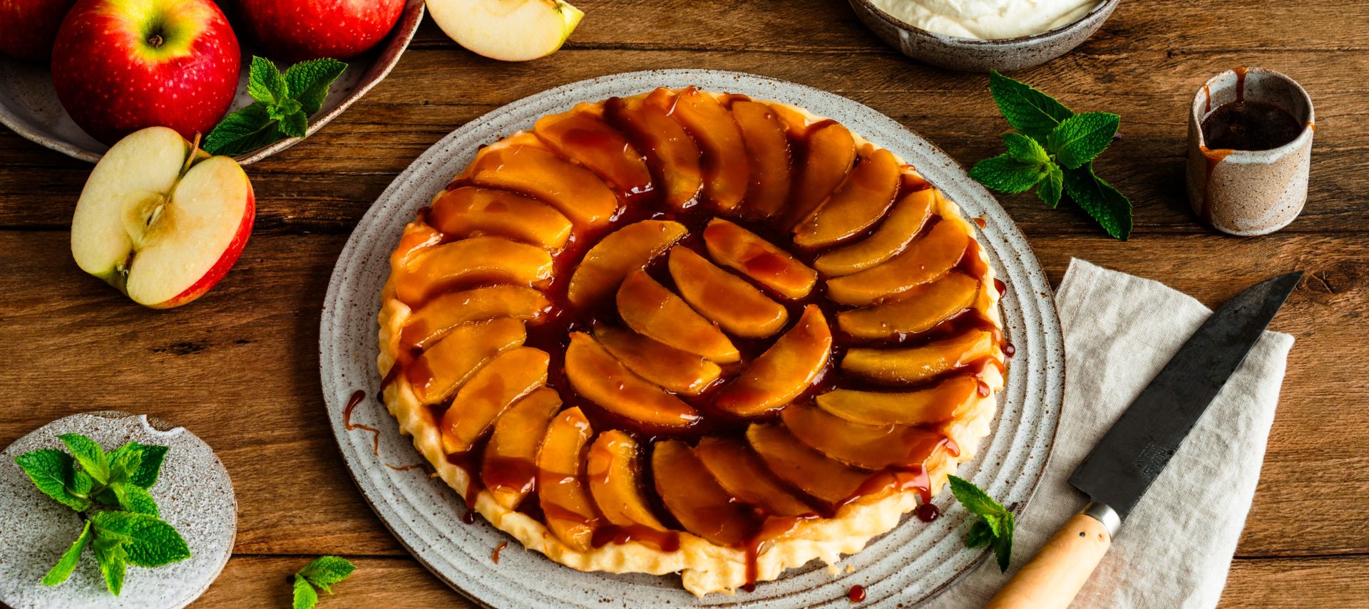 Ein rundes Apfel-Tarte-Tatin auf einem Keramikteller, belegt mit glänzend karamellisierten Apfelscheiben in konzentrischen Kreisen.