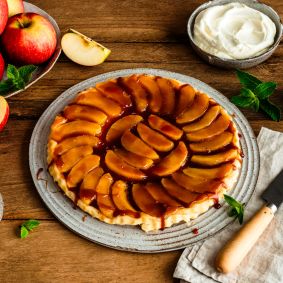 Ein rundes Apfel-Tarte-Tatin auf einem Keramikteller, belegt mit glänzend karamellisierten Apfelscheiben in konzentrischen Kreisen.