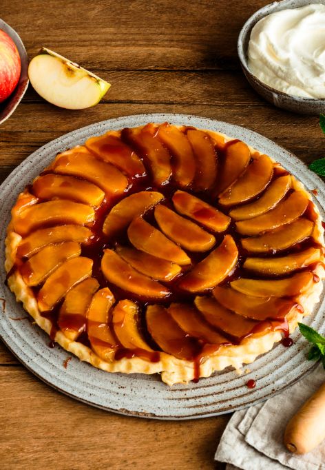 Ein rundes Apfel-Tarte-Tatin auf einem Keramikteller, belegt mit glänzend karamellisierten Apfelscheiben in konzentrischen Kreisen.